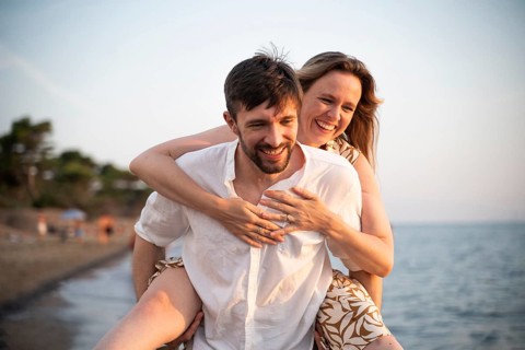 A joyful couple enjoys a playful day at an Italian beach, with one partner giving the other a