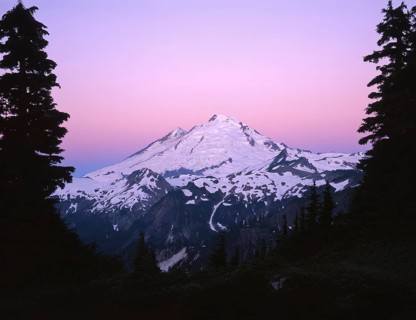 A stunning view of a snow capped mountain silhouetted against a vibrant pink and purple sky at