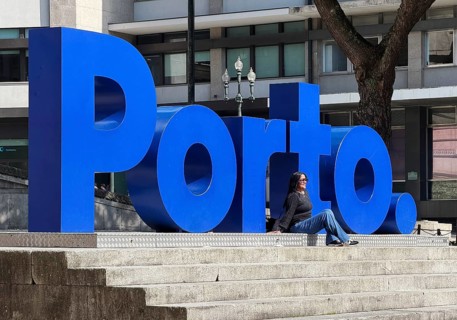 A woman is photographed in front of the big blue Porto logo at City Hall, Câmara Municipal do