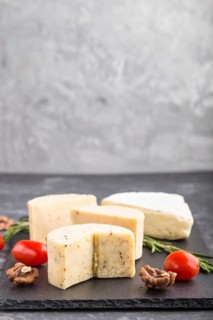 Cheddar cheese and various types of cheese with rosemary and tomatoes on black slate board on a
