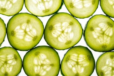 Fresh cucumber slices arranged in a seamless pattern against a crisp white background. The vibrant
