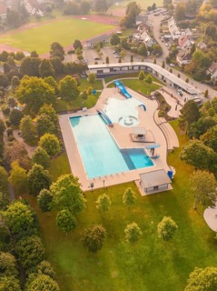 A swimming pool with outdoor area, surrounded by green spaces and trees, in an urban environment