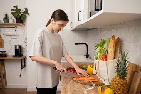 Teenage girl cuts fresh vegetables on a wooden countertop in a modern kitchen. Nearby are