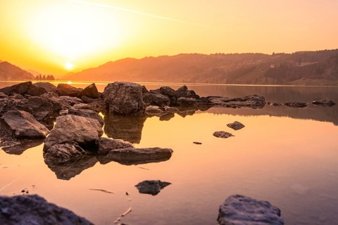 Rocks on the shore of a lake reflect the warm light of sunset, Großer Alpsee, Immenstadt im Allgäu,