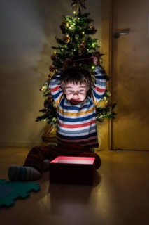 A young boy is sitting in front of a Christmas tree with a red box in front of him