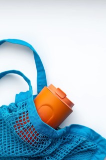 Top view of an orange thermo cup nestled in a vibrant blue mesh reusable bag, emphasizing an