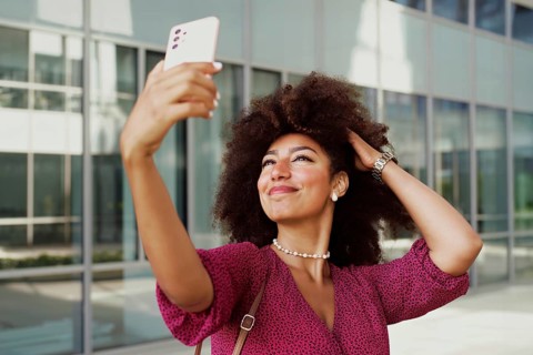A young Arab woman smiles confidently while capturing a selfie using her smartphone outside a