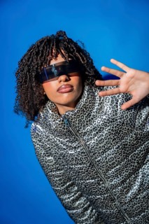 Stylish model showcasing futuristic eyewear and a trendy animal print jacket against a vibrant blue