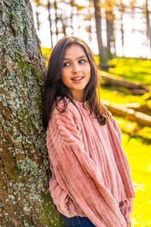 Vertical side view portrait of a caucasian cute girl leaning in a tree trunk in the forest