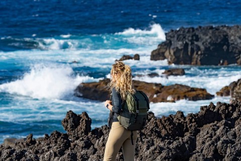 A woman with a backpack enjoys the rugged volcanic coastline at Timanfaya National Park, Lanzarote.