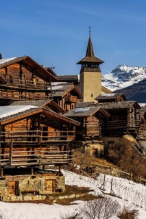 Snow-covered roofs of old farmhouses and barn storage, in the back the church tower of the Saint