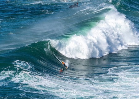 Surfers with their jet ski pilots in the Atlantic waves below Farol de Nazaré, Forte São Miguel,