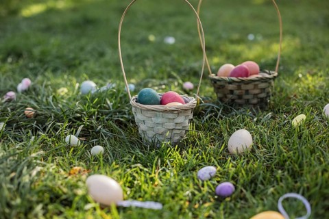 Wicker baskets filled with colorful Easter eggs sit in the lush grass, surrounded by scattered eggs