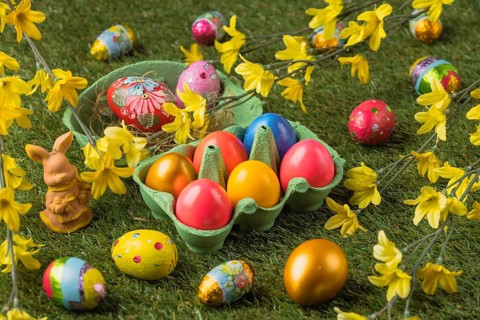 Colourful Easter eggs next to a small Easter bunny figure surrounded by bright blossoms