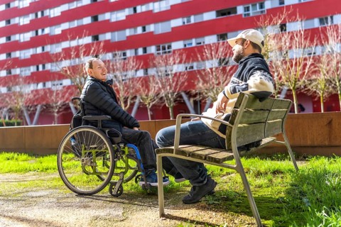 Two men relaxing on a bench in a city park, enjoying conversation and sunshine, demonstrating the