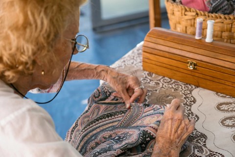 Elderly seamstress is meticulously sewing a piece of paisley fabric with a needle and thread, her