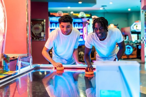 Two young men enjoying an exciting game of air hockey in a lively amusement arcade, surrounded by