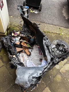 A picture of a heavily melted rubbish bin that has obviously been damaged by fire. The plastic is