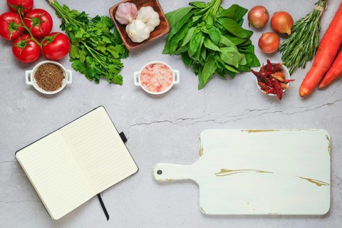 Diet food concept of healthy eating. Opened notebook next to cutting board and fresh vegetables and