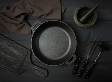Cast iron brazier, with cooking utensils, for cooking, on a dark gray, wooden table, top view,
