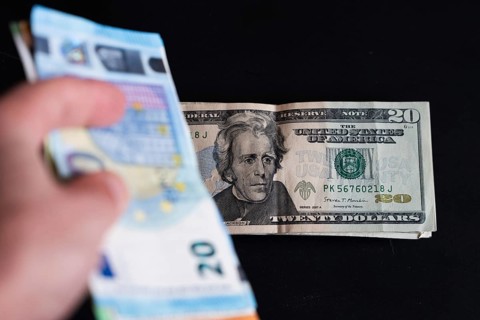 20 dollar banknotes on a black background and in the foreground 20 euro banknotes held in a hand in