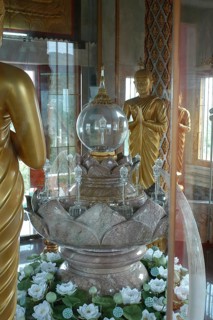 Praying Buddha statues and stylised lotus blossom in relic room with relics under glass in dome of