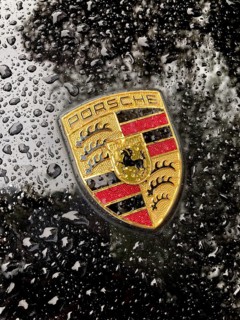 Porsche crest on black bonnet of sports car with sparkling raindrops, international