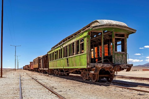 Rusty green passenger car rots in a sunny desert landscape, railroad cars in the town of Ollagüe in