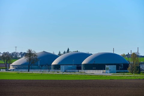 Agricultural biogas plant with three domes in green surroundings under blue sky, Middle Franconia,