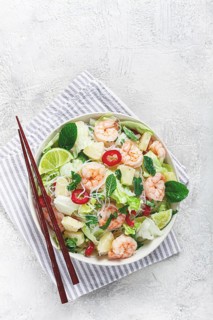 Thai salad with shrimp and rice noodles, pineapple slices, coriander and mint leaves, on a white