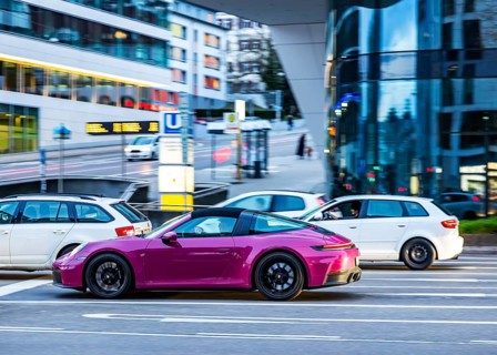 Car at night in front of an urban environment with modern architecture, driver. Purple Porsche 911.
