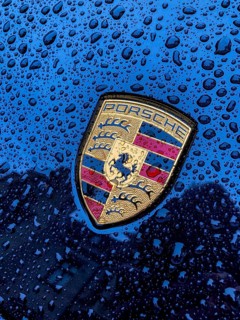Porsche crest on navy blue bonnet of sports car with sparkling raindrops, international