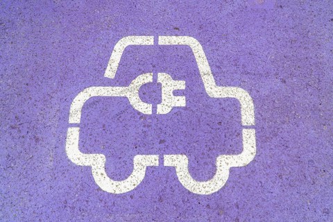 Close-up of a white electric vehicle EV charging station symbol painted on a purple asphalt