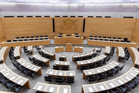 Plenary hall deserted with the seats of deputies and the government bank. Behind it is the coat of