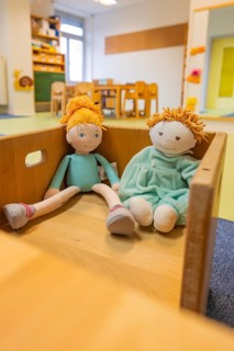 Two dolls in a wooden box, placed in a child-friendly room with colorful interior, infant and