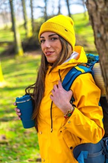 Hiker enjoying a hot drink in the woods during a trekking day, wearing yellow raincoat and backpack