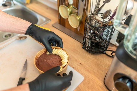 Chef hands wearing black gloves arranging sliced bananas on top of a chocolate smoothie bowl,