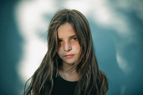 A serene portrait of a teen girl standing in soft tree shadows. The gentle lighting highlights her