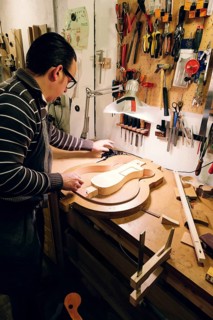 A luthier meticulously crafts a bass guitar in a workshop filled with tools. The intricate process