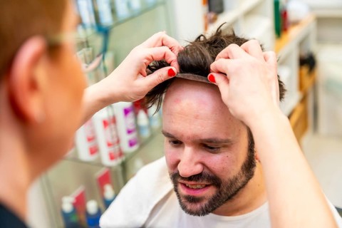 Close-up top view of a hairdresser placing a capillary prosthesis carefully to a man's head