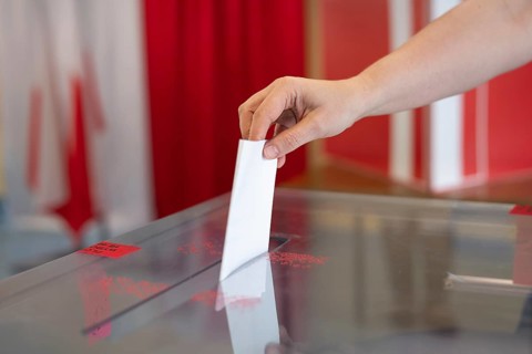 Voter's hand putting the vote into the ballot. Polish flag and emblem in the background
