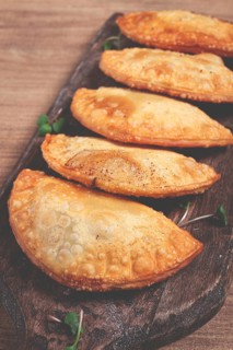 Fried chebureks, deep-fried, mini, on a chopping board, wooden table, close-up, no people