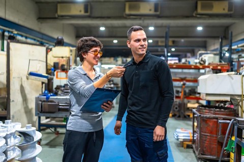 Female manager of factory talking and giving orders to male worker while holding clipboard