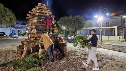 Men stacking wood at night, surrounded by trees and lantern light, Easter fire Psinthos, Holy