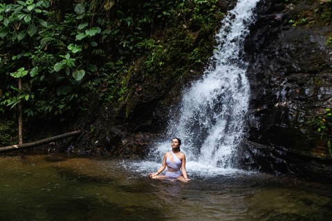 Young woman from Ecuador meditating at a serene waterfall pool in the lush Choco Andino rainforest