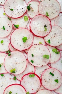 Thinly sliced radishes in vibrant red and white colors are arranged on a white surface, sprinkled