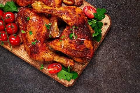 Grilled fried chicken legs, served with fresh cherry tomatoes, and herbs, on a wooden chopping