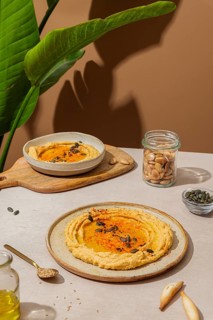 A rustic table setting featuring creamy hummus drizzled with olive oil and sprinkled with seeds.