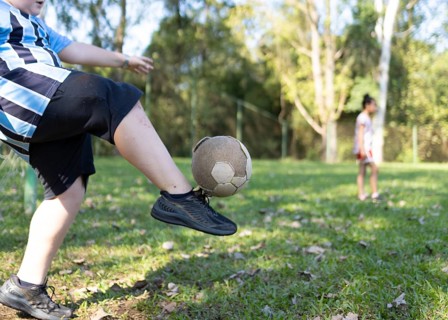 Cropped unrecognizable Brazilian children play soccer on a lush grass field in Tres Coroas, Brazil.