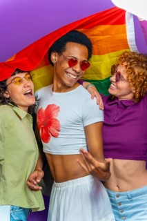 Studio portrait with purple background of a gay man and two lesbian women dancing covered by lgbt